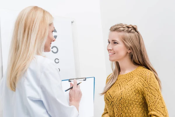 Patient and oculist with diagnosis and eye chart behind — Stock Photo