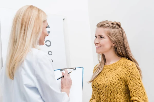 Patient et oculiste avec diagnostic et tableau oculaire derrière — Photo de stock