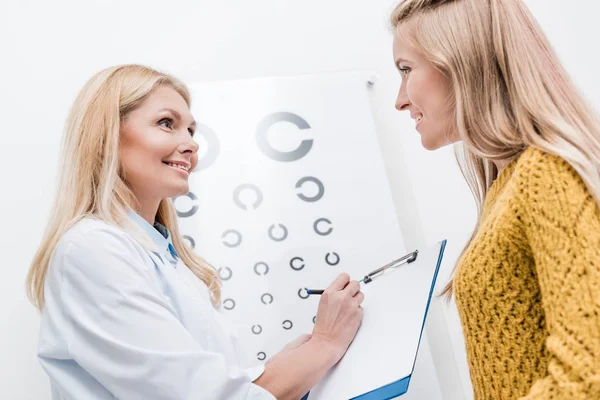 Paciente y oculista con diagnóstico y gráfico ocular detrás - foto de stock