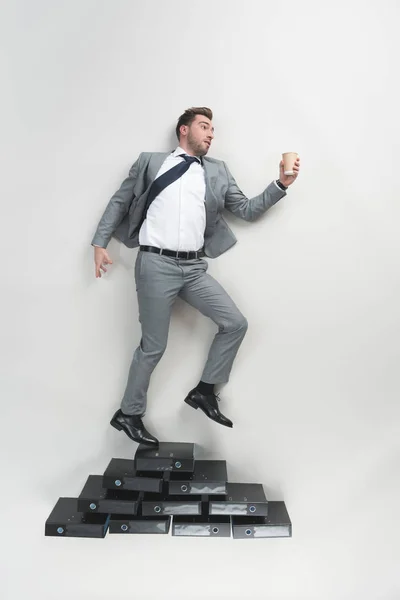 Overhead view of businessman with coffee to go in hand standing on pile of folders isolated on grey — Stock Photo