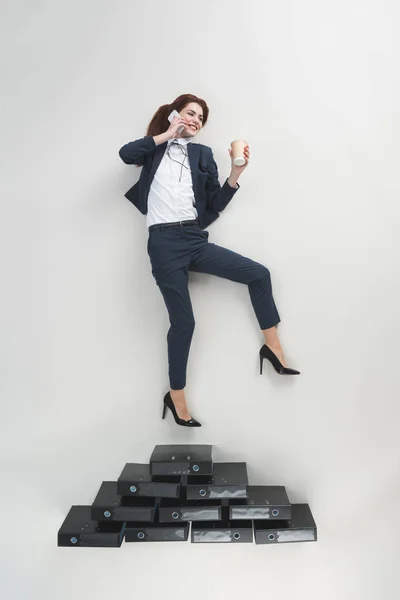 Blick von oben auf lächelnde Geschäftsfrau mit Kaffee to go in der Hand, die auf dem Smartphone isoliert auf grau spricht — Stockfoto