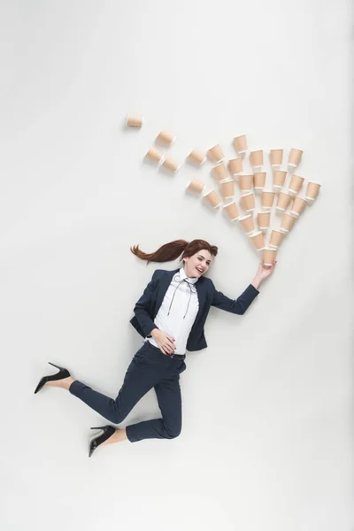 Vue aérienne d'une femme d'affaires joyeuse avec des tasses jetables isolées sur gris — Photo de stock