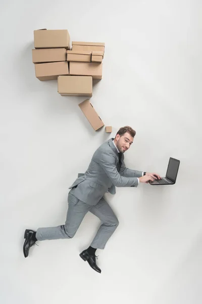 Vista aérea del hombre de negocios con cajas de cartón por encima de la cabeza utilizando el ordenador portátil aislado en gris - foto de stock