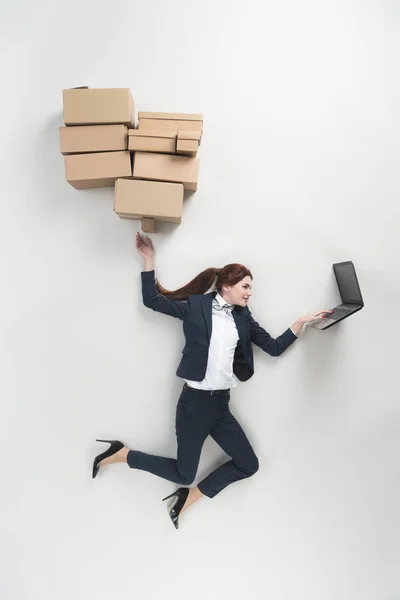 Overhead view of businesswoman with cardboard boxes using laptop isolated on grey — Stock Photo