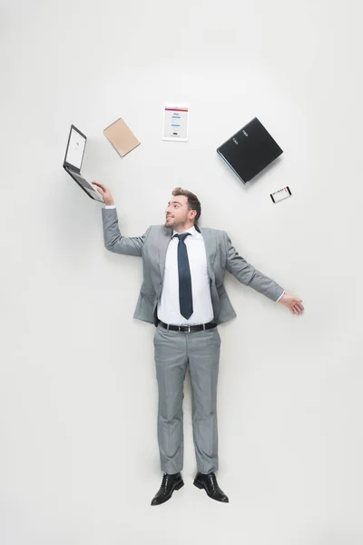 Overhead view of businessman with office supplies above head using laptop isolated on grey — Stock Photo