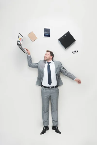 Vista aerea di uomo d'affari con forniture per ufficio sopra la testa utilizzando laptop isolato su grigio — Foto stock