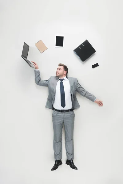 Vista aérea del hombre de negocios con suministros de oficina por encima de la cabeza utilizando el ordenador portátil aislado en gris - foto de stock