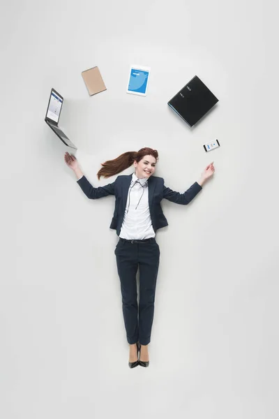 Vista aérea de la mujer de negocios con varios suministros de oficina utilizando el ordenador portátil aislado en gris - foto de stock