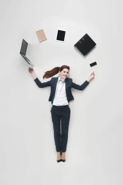 Vista aérea de la mujer de negocios con varios suministros de oficina utilizando el ordenador portátil aislado en gris - foto de stock