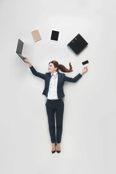 Vista aérea de la mujer de negocios con varios suministros de oficina utilizando el ordenador portátil aislado en gris - foto de stock