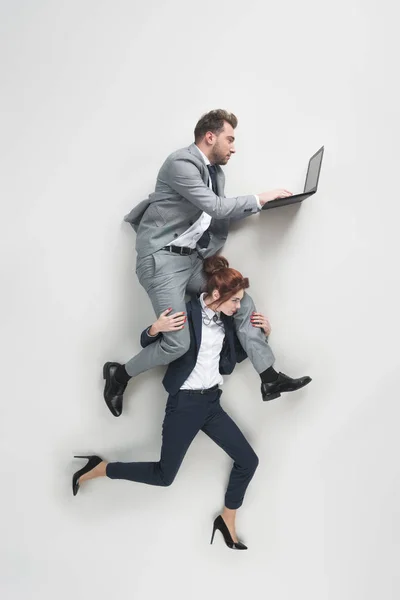 Vista aérea de la mujer de negocios que lleva hombre de negocios que trabaja en el ordenador portátil aislado en gris - foto de stock