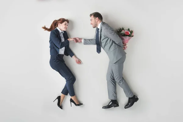 Overhead view of smiling businessman going to present flowers to colleague isolated on grey — Stock Photo