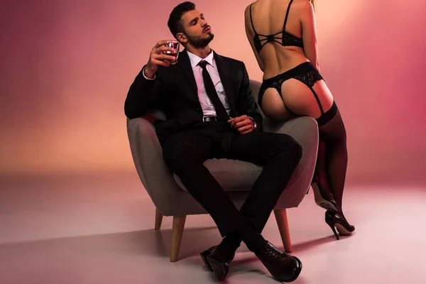 Bonito empresário sentado no poltrona com sexy menina no lingerie — Fotografia de Stock