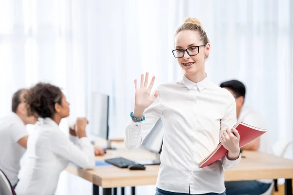 Young caucasian student girl waving hand in classroom with friends — Stock Photo