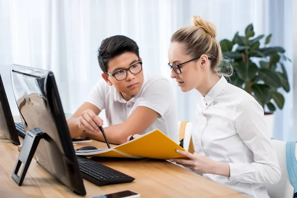 Joven estudiante serio apuntando en el libro de ejercicios a su compañero de clase - foto de stock