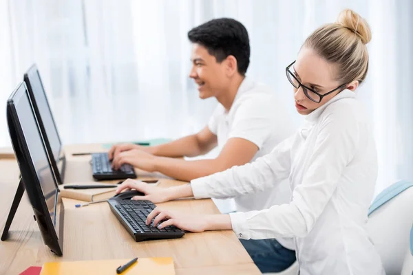 Jóvenes estudiantes adolescentes que trabajan en computadoras, chica hablando en el teléfono inteligente - foto de stock