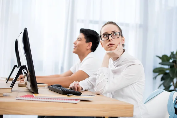 Nachdenkliche junge Studenten sitzen am Tisch und schauen sich etwas an — Stockfoto