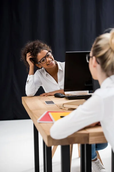 Dos adolescentes estudiante niñas sentado en la mesa y mirándose entre sí - foto de stock