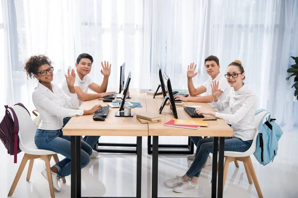 Seitenansicht von vier jungen multikulturellen Studenten, die in die Kamera schauen und winken — Stockfoto