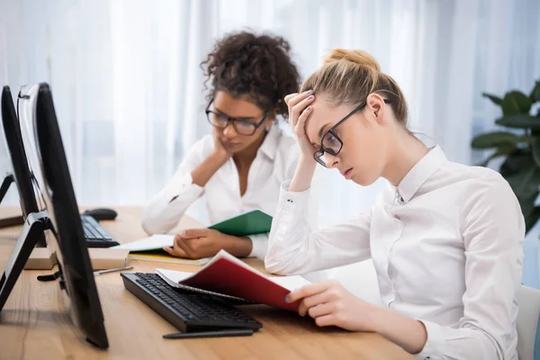 Young tired teenager girls studying on computers with exercise books — Stock Photo