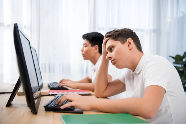 Jóvenes chicos adolescentes cansados estudiando en computadoras - foto de stock