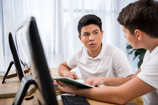 Joven estudiante serio apuntando en el libro de ejercicios a su compañero de clase - foto de stock