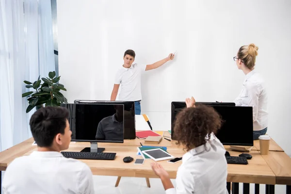 Jovem adolescente apontando no quadro branco em sala de aula com os alunos — Fotografia de Stock