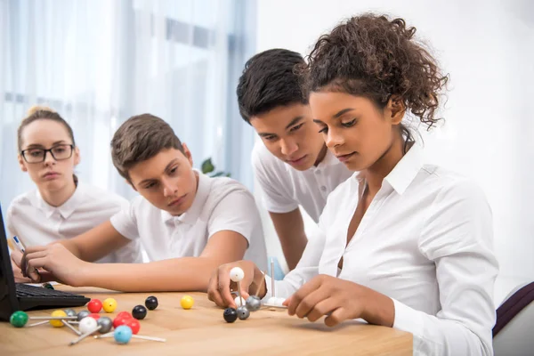 Jeunes étudiants multiculturels choisissant un modèle moléculaire pour une leçon de chimie — Photo de stock