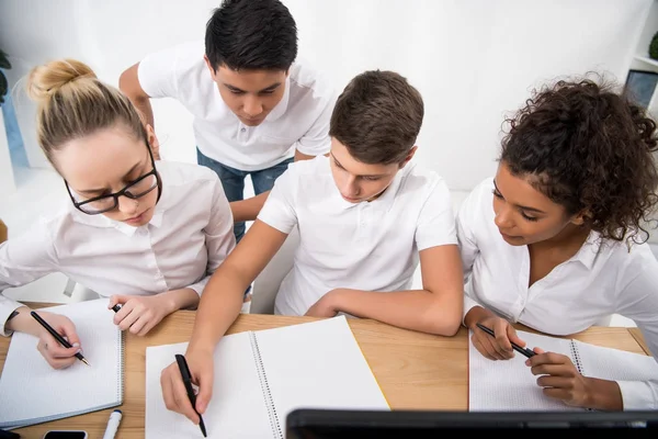 Jóvenes estudiantes que escriben algo en cuadernos - foto de stock