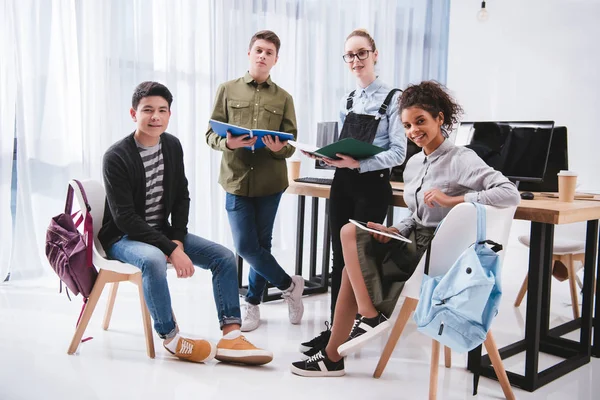 Cheerful young students with exercise books and tablet looking at camera — Stock Photo