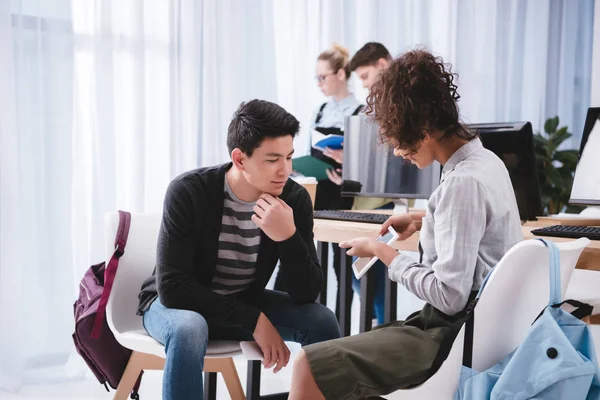 Joven africano americano estudiante mostrando algo en tableta a asiático chico - foto de stock