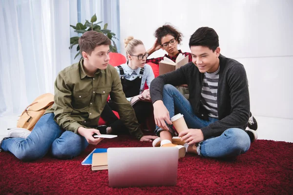 Adolescentes multiculturales que estudian con computadora portátil y libros de ejercicios - foto de stock