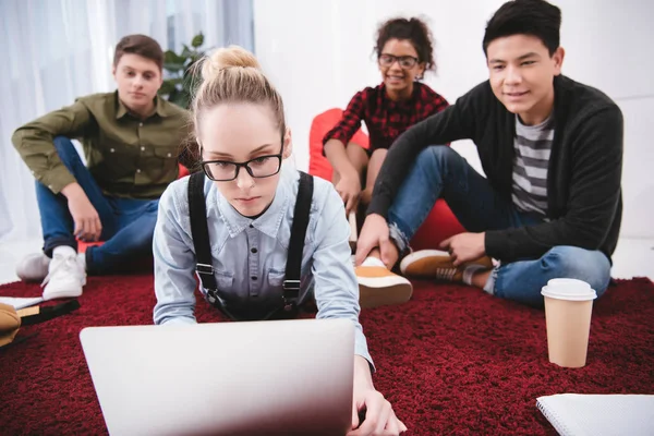 Jóvenes estudiantes adolescentes acostados en la alfombra con cuadernos y mirando a la computadora portátil - foto de stock