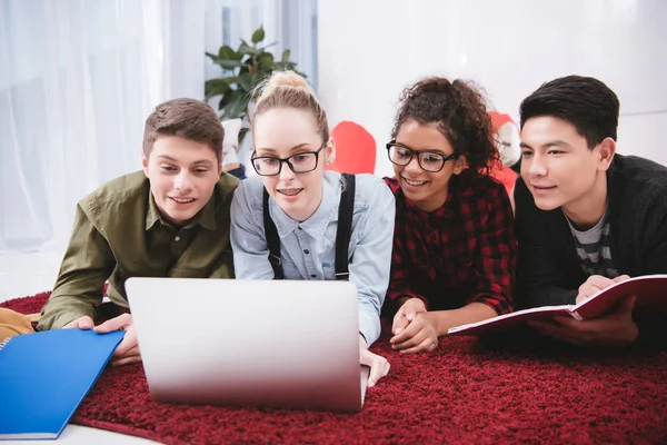 Jugendliche Studenten liegen mit Notizbüchern auf Teppich und schauen auf Laptop — Stockfoto