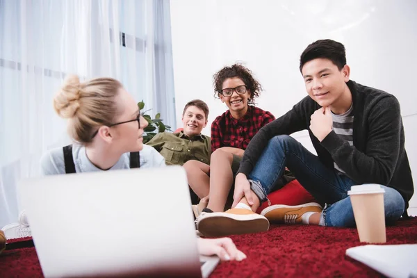 Young teen students lying on carpet with notebooks and looking at laptop — Stock Photo