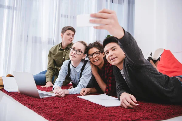 Young teen students lying on carpet and taking selfie — Stock Photo