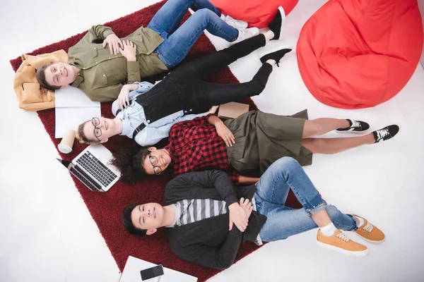 Молоді студенти-підлітки лежать на килимі з блокнотами та ноутбуком — стокове фото
