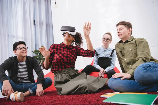 Young girl in virtual reality glasses sitting on carpet with friends — Stock Photo