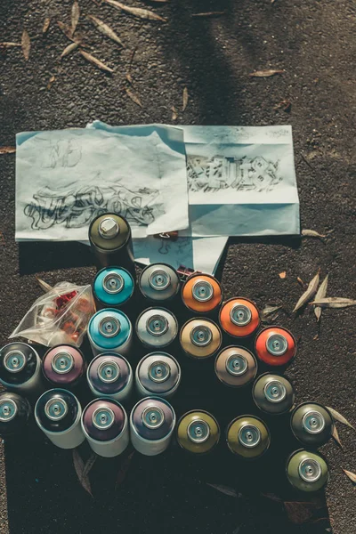 Top view of graffiti sketches and cans with colorful spray painton asphalt — Stock Photo