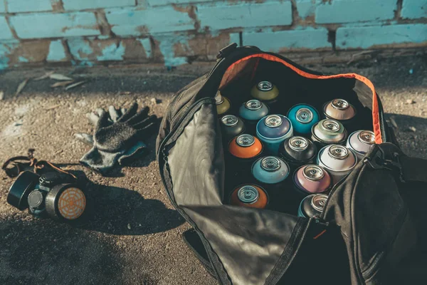 Luvas e respirador perto de saco grande com latas de tinta spray — Fotografia de Stock