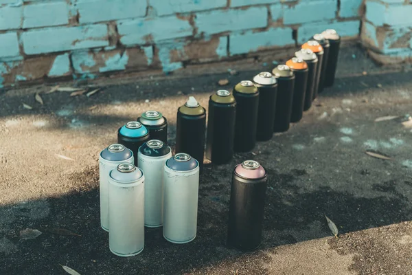 Cans with aerosol paint standing in row on asphalt — Stock Photo