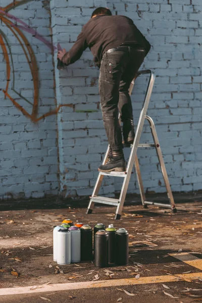 Uomo in piedi sulla scala e pittura graffiti colorati sulla costruzione — Foto stock