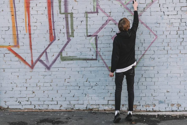 Visão traseira do homem pintando graffiti colorido na parede — Fotografia de Stock