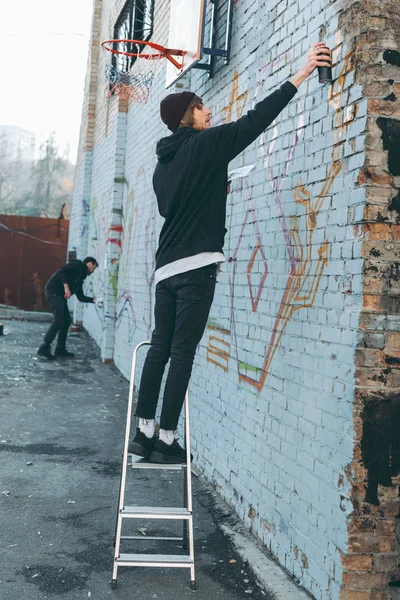 Homem em pé na escada e pintura graffiti colorido na construção — Fotografia de Stock