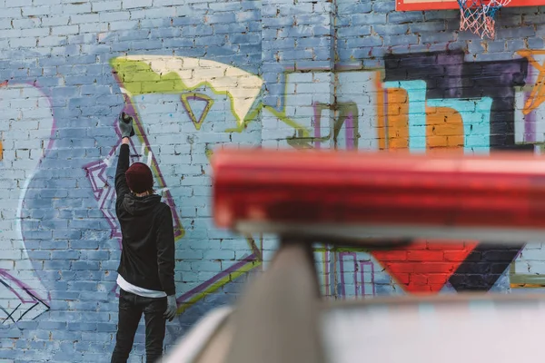 Visão traseira de grafite pintura vândalo na parede, carro de polícia em primeiro plano — Fotografia de Stock