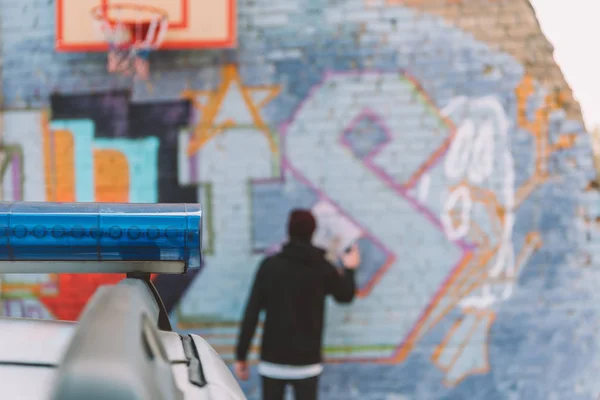 Vue arrière des graffitis de peinture vandale sur le mur, voiture de police au premier plan — Photo de stock