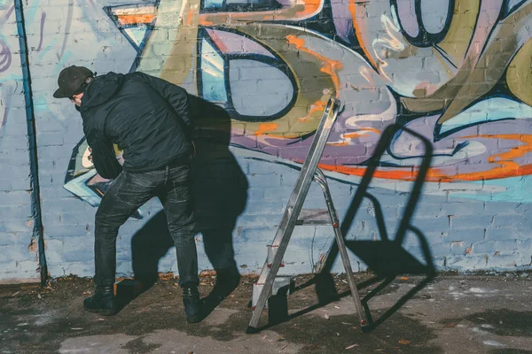 Artista callejero pintando graffiti colorido en la pared del edificio - foto de stock