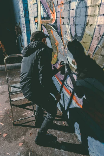 Человек рисует красочные граффити на стене здания ночью — стоковое фото