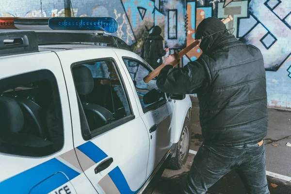 Vandal crashing police car with baseball bat while another man painting graffiti on wall — Stock Photo