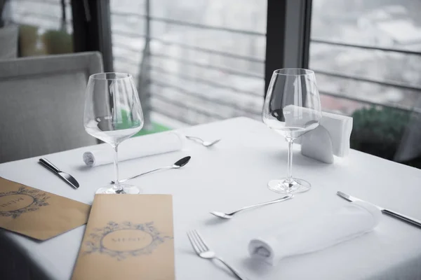 Vue rapprochée des couverts arrangés, verres à vin vides et menu sur table avec nappe blanche au restaurant — Photo de stock